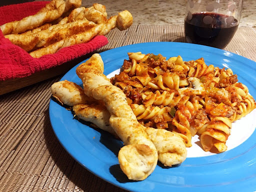 A couple breadsticks on a plate with pasta.