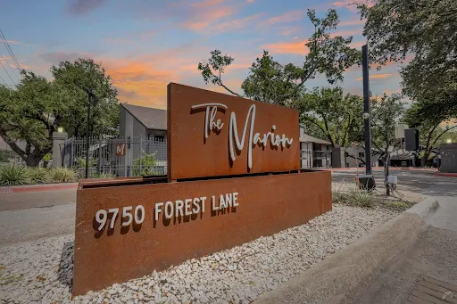 Sign for The Marion apartment complex with address 9750 Forest Lane, surrounded by greenery and a colorful sunset.