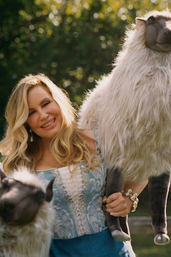 Jennifer Coolidge holding two sheep, one under her arm and another over her shoulder.