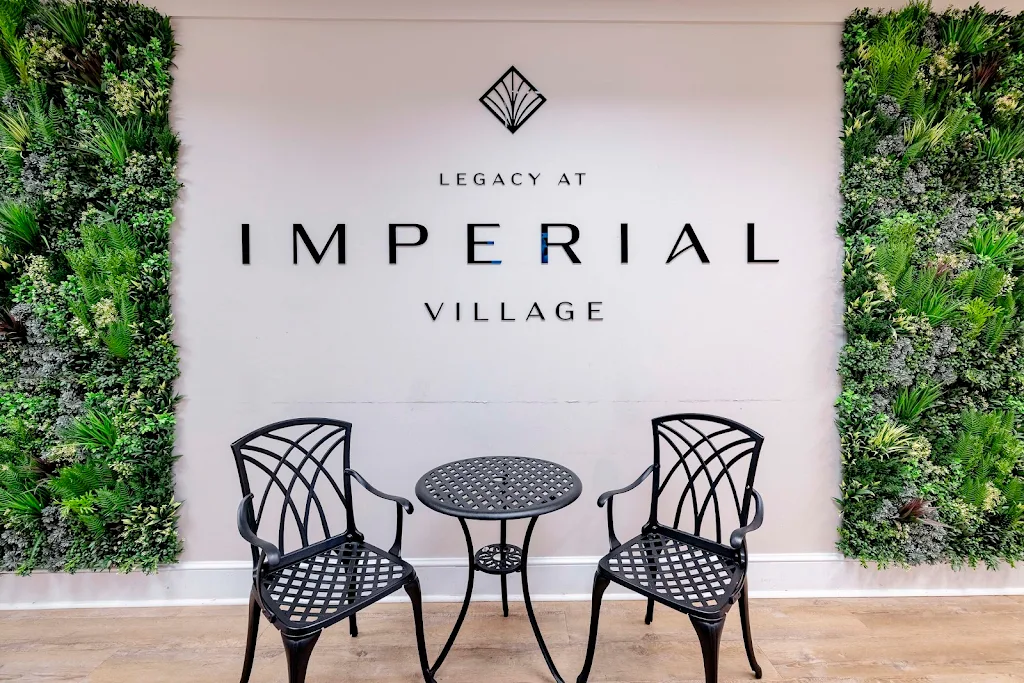 Lobby of Legacy at Imperial Village apartment complex with logo, two chairs, table, and green wall foliage.