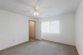 Bedroom with carpeted flooring, window with blinds, white walls, and a ceiling fan overhead 