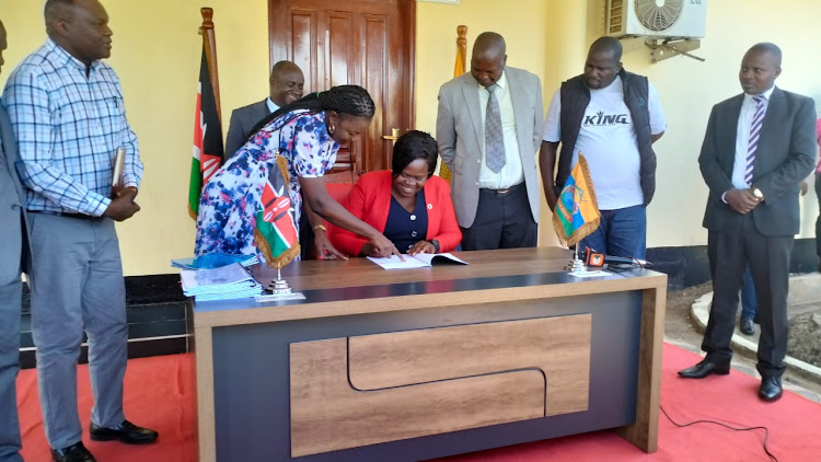 Homa Bay county assembly clerk Faith Apuko shows Governor Gladys Wanga where to sign during signing and sealing of four municipality charters in Homa Bay town on January 9, 2023.