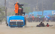 Passengers use a rope to wade through flood water along a street as they get evacuated from a public transport bus following heavy rains in Kisauni district of Mombasa, Kenya, on November 17 2023.