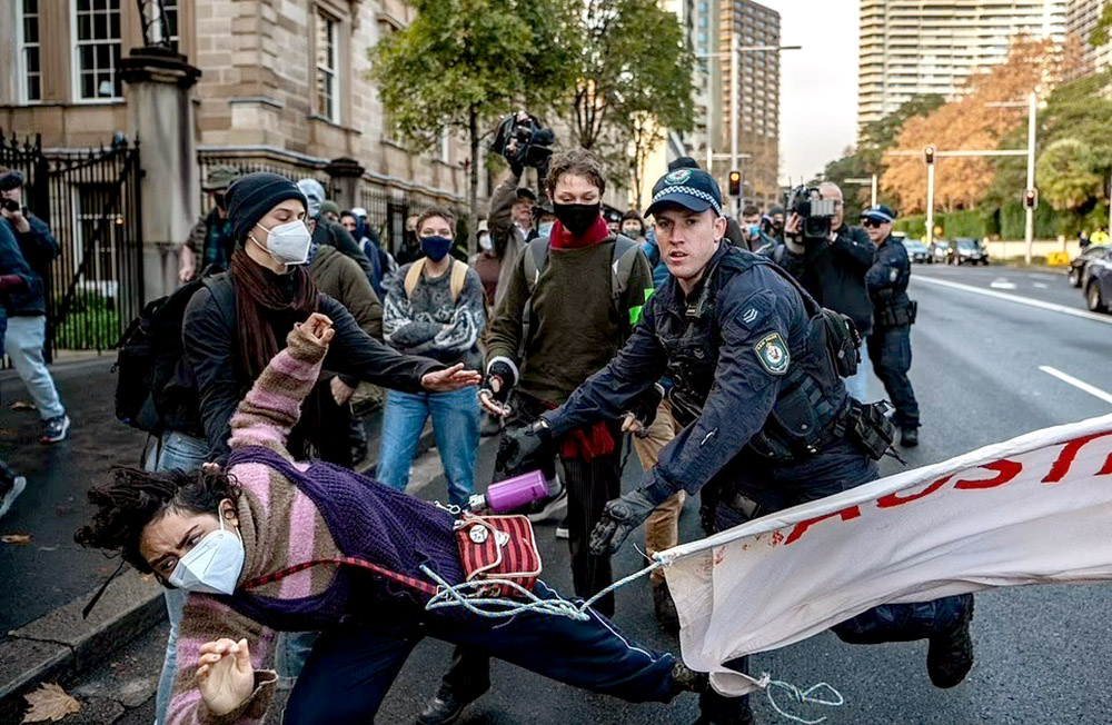 An activists is mid fall on a tarmac road, the police office still in the process of pushing them to the ground