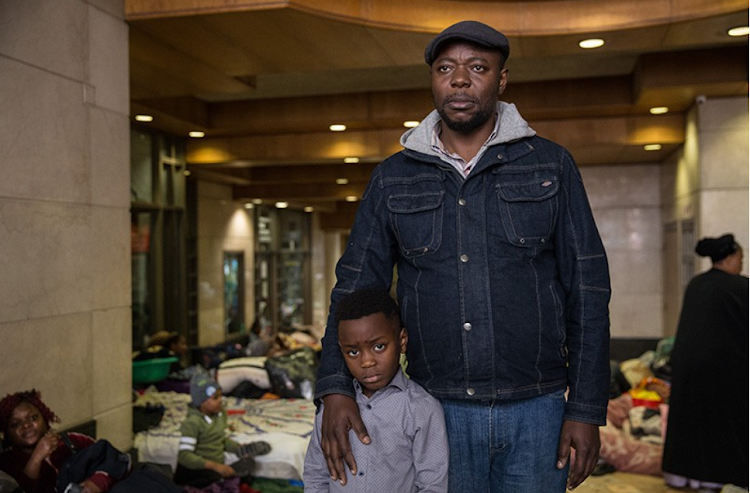 Kande-Serge Kande stands with his son pleading for the UNHCR to let refugees leave SA. (Publication of photo approved by Kande)