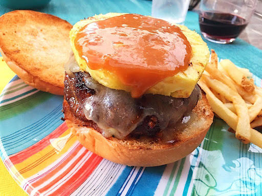 A grilled burger topped with a pineapple slice and a teriyaki sauce.