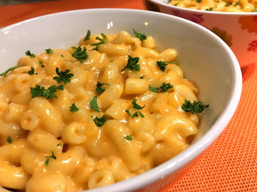 Two bowls of macaroni and cheese sitting on an orange table mat.