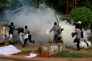 Protesters run from tear gas thrown by the police during a June 12 Democracy Day rally in Abuja, Nigeria, on June 12 2021. 