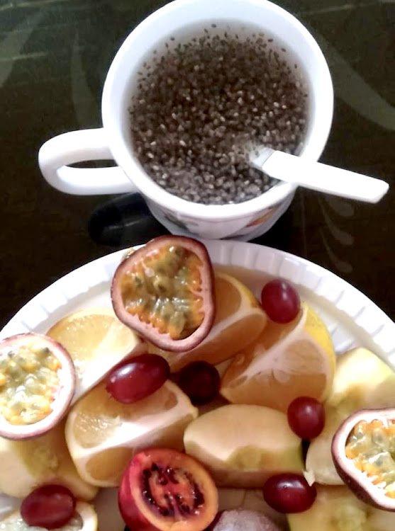 A cup of water mixed with chia seeds, next to a plate of mixed fruits