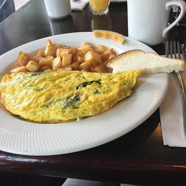 Omelet filled with cheese and spinach, hash browns and bread. (The bread is on an extra plate so there are more than one slice)