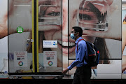 A person wearing a protective face mask walks past a tram with a public health sign asking people to wear masks in Sydney, Australia, December 10, 2020.  