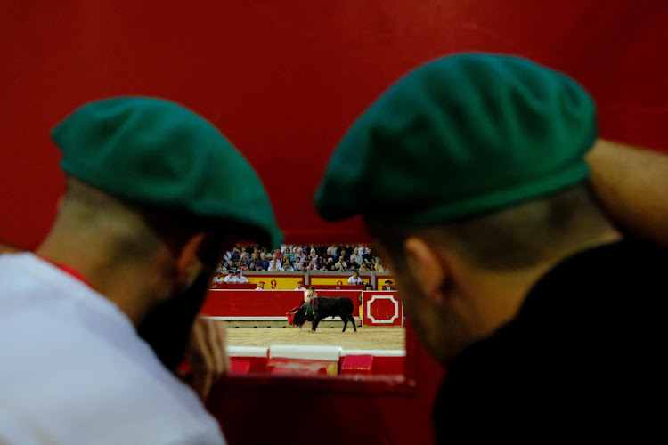 Two bullring workers watch novice bullfighter Marcos Linares during a bullfight in Pamplona, Spain.