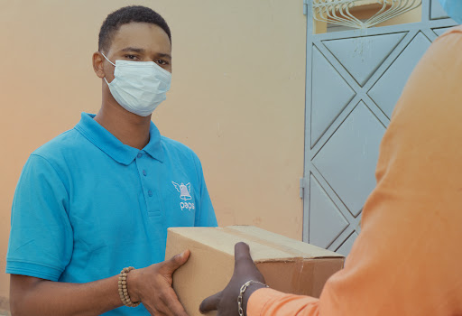 A Paps delivery person wearing a mask delivers a package to a customer.