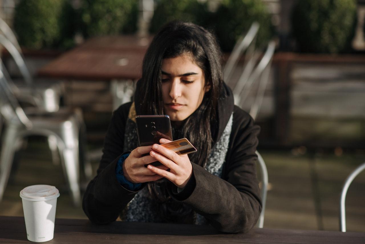 A teenager holding a debit card and using his phone