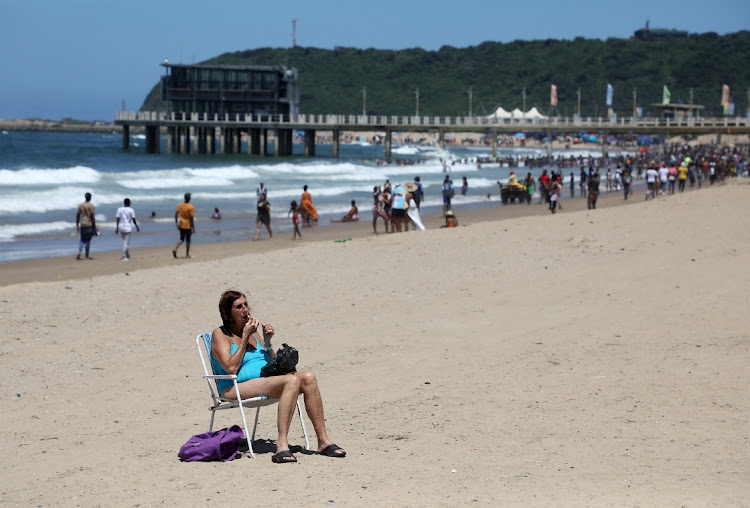 A woman puts on a lipstick while enjoying the sun at the uShaka Marine beach in Durban.