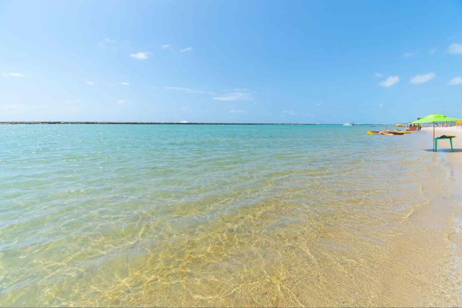 Águas cristalinas e azuladas de uma praia em Recife, e algumas pessoas ao fundo.