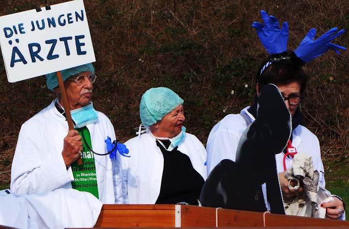 Drei als nicht mehr ganz junge Mediziner Vermummte mit Schild «Die jungen Ärzte».