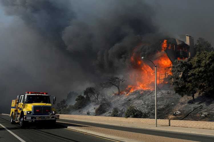 A fire crew passes a burning home during a wind-driven wildfire in Ventura, California, U.S. on December 5, 2017.