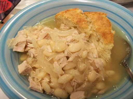 Bowl containing cooked October Beans with Pork Tenderloin and Onion in broth with Cornbread wedges.