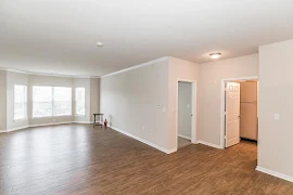 Living area with neutral walls, white trip, wood-inspired flooring, and large bay windows with hallway leading to bedroom