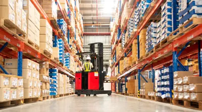 A warehouse worker is operating forklifts in a warehouse filled with boxes.