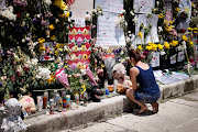 A woman kneels at a memorial site created by neighbors in front of a partially collapsed residential building as the emergency crews continue the search and rescue operations for survivors, in Surfside, Florida, US July 3, 2021. 