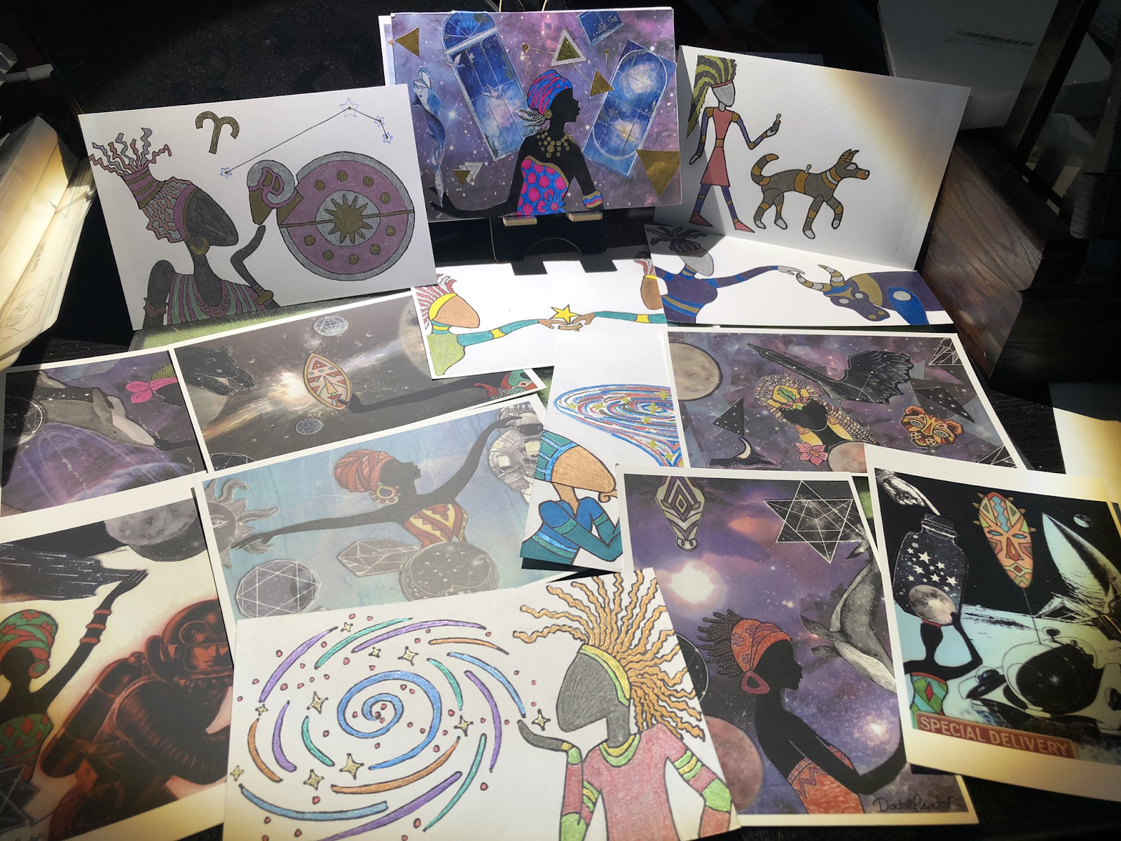 A series of postcards spread out on a table featuring African-inspired designs and colorful purple cosmos.