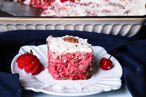 A slice of Cherry-Berry Cake on a plate with sprinkled coconut, strawberries, and a cherry.