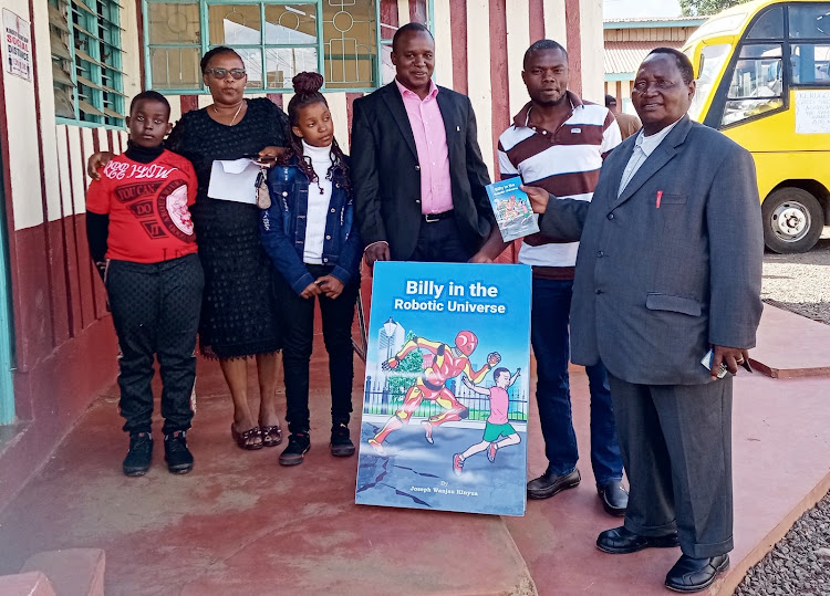 Joseph Wanjau parents(father in pink shirt and mother in black dress),younger siblings and teachers poses for a photo with a dummy and a real copy of a book authored by the young candidate.