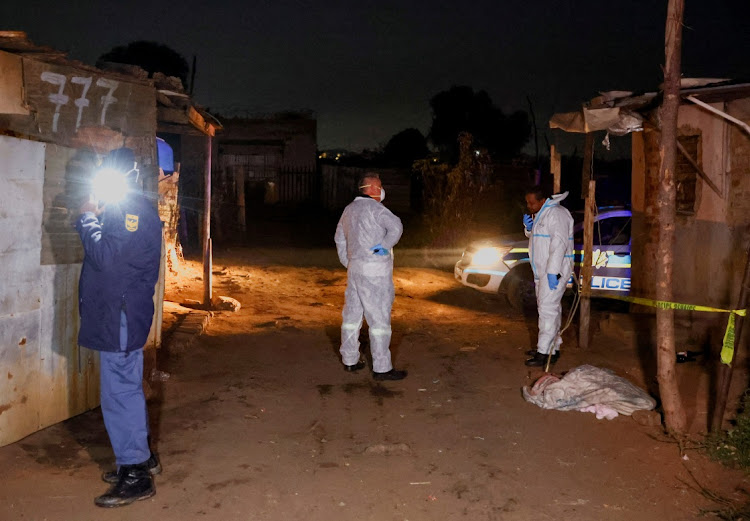 A police officer and forensic team members stand near the body of a child covered by a piece of cloth at the scene of a suspected gas leak thought to be linked to illegal mining.