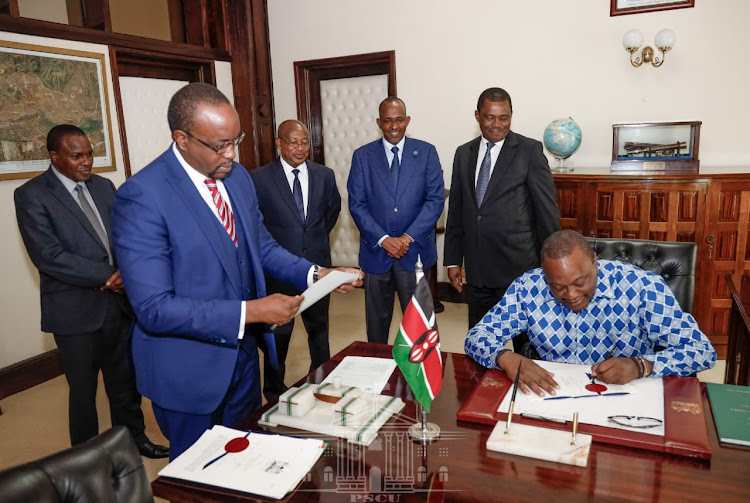 President Uhuru Kenyatta signs a bill as speaker Justin Muturi, Majority leader Aden Duale and other officials look on.