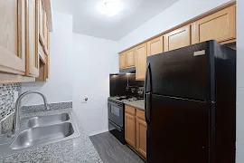 Compact kitchen with stainless steel sink, black appliances, wooden cabinets, and mosaic backsplash in an apartment.