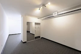 Carpeted bedroom with overhead lighting, white walls, and a closet with a sliding door and mirror