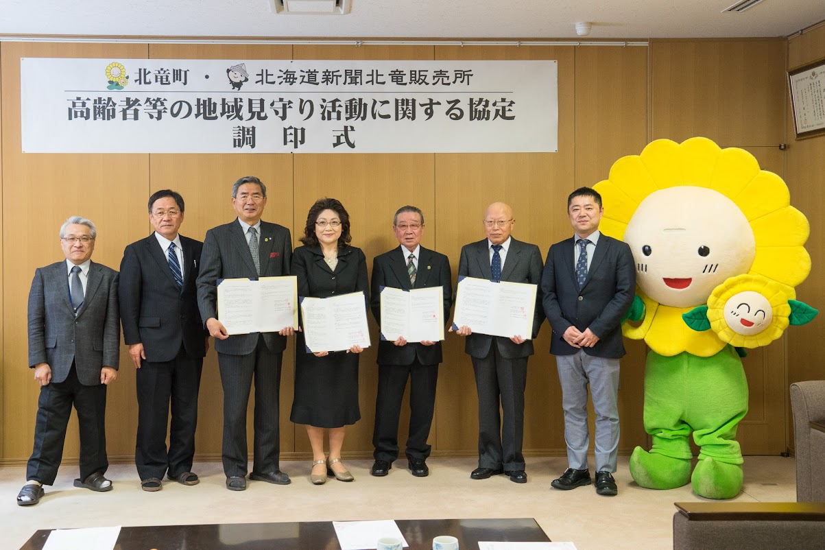  左より：北竜町住民課・中村道人 課長、竹内範行 副町長、佐野豊 町長、旭川地方道新会深川留萌地区会・倉本茂子 会長、北海道新聞有馬販売所・有馬昌志 様、北海道新聞佐崎販売所・佐崎謙次 様、北海道新聞社旭川支社・梅内竜也 様、ひまわり咲ちゃん