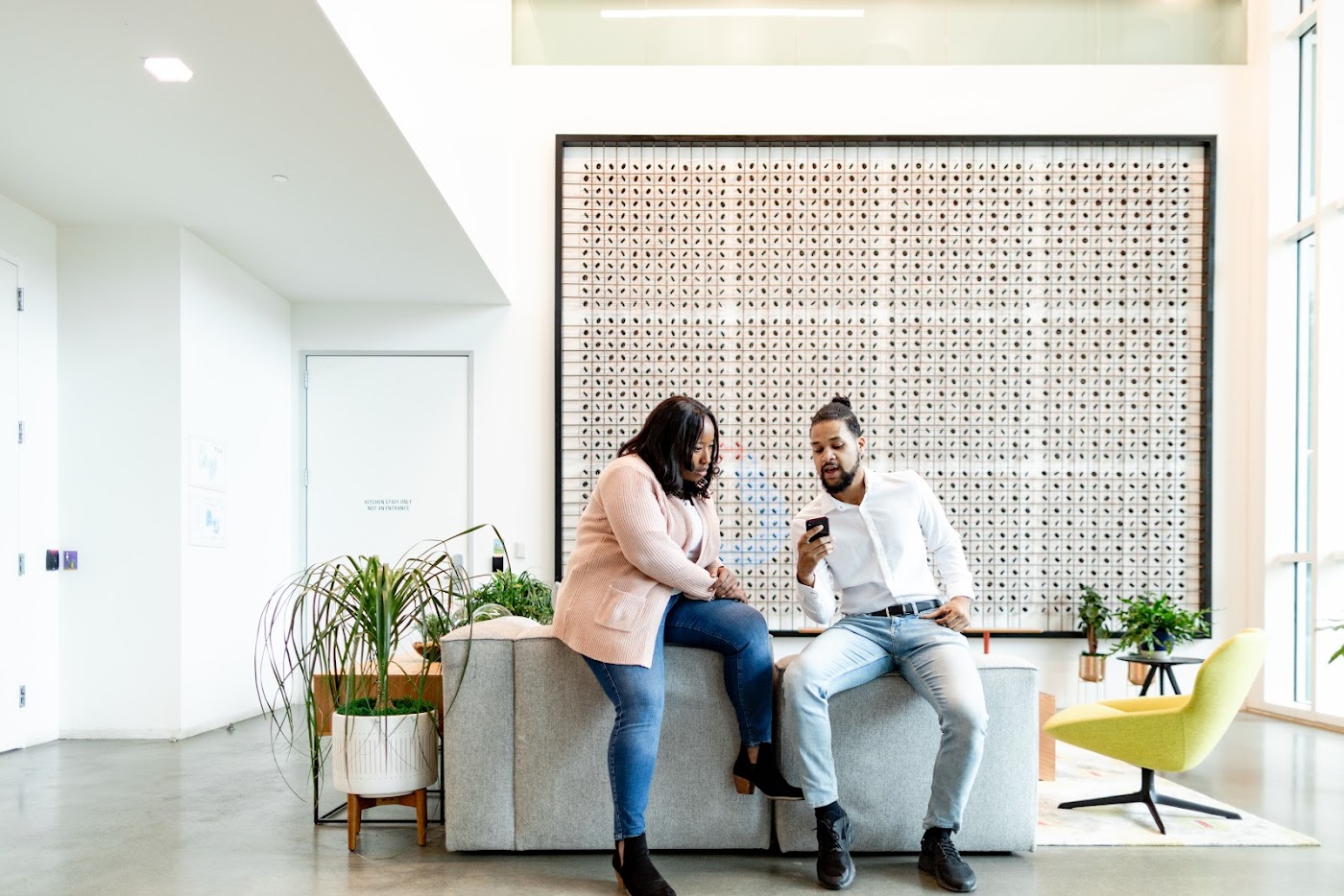 A man and woman wearing casual clothes sit at a desk at work, talking.