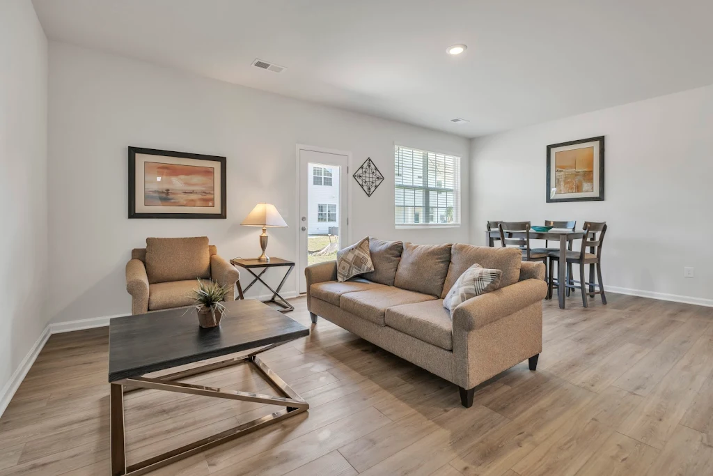 Model townhome living room area with furniture, wood finish flooring, and bright white neutral color scheme