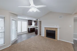 Living room with carpet, fireplace, vaulted ceiling, and views into the dining and kitchen areas.