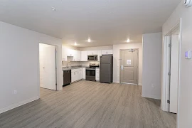 Open concept living room with wood-inspired flooring, view of the kitchen area, and neutral colored walls