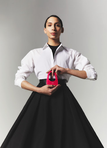 Charles Gross in a white dress shirt and a black dress holding a pink Coperni mini bag.