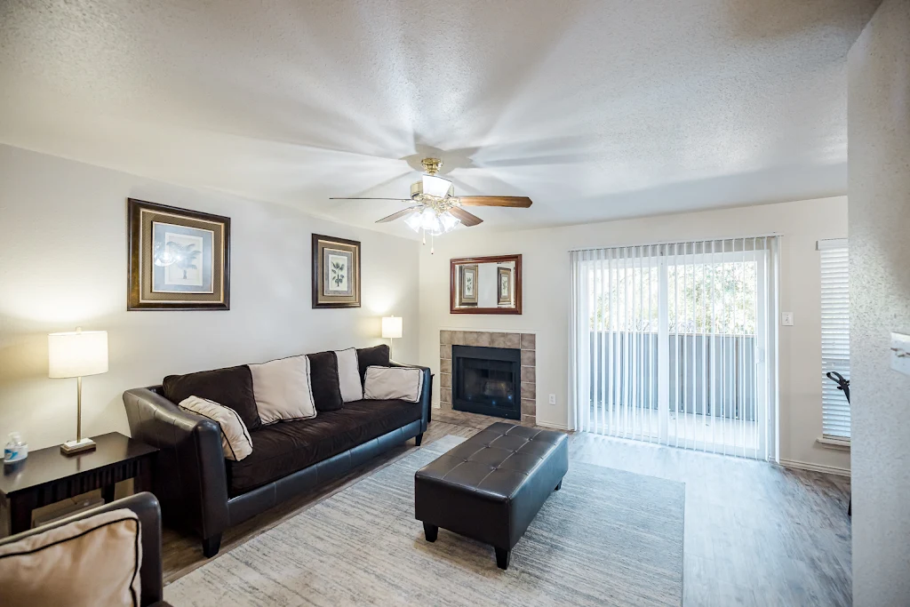 Furnished living room with wood-inspired flooring, sliding glass patio door with blinds, ceiling fan, and tiled fireplace