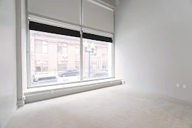 Bedroom with light carpet and large floor-to-ceiling windows with solar shades