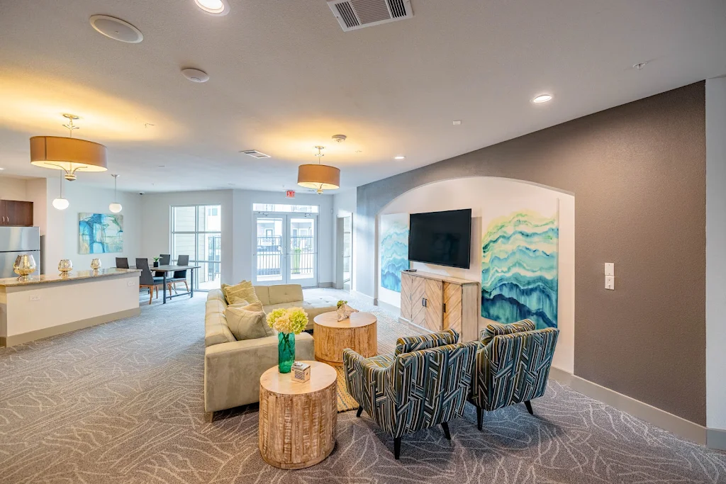 Resident lounge with TV, seating areas, dining table with chairs, and full kitchen