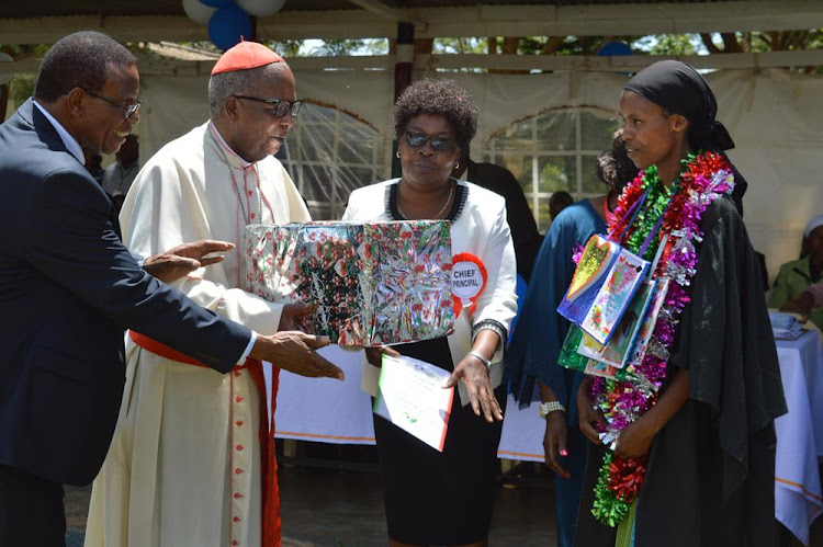 Archbishop John Cardinal Njue handing a present to Margret Wangeci (right) who emerged the best overall student graduating in the 71st graduation ceremony of St. John's teachers training college Kilimambogo Kiambu county as Chief Principal Damaris Mbogo and the institute Board of management chairman Lawrence Kungu (left) looks on