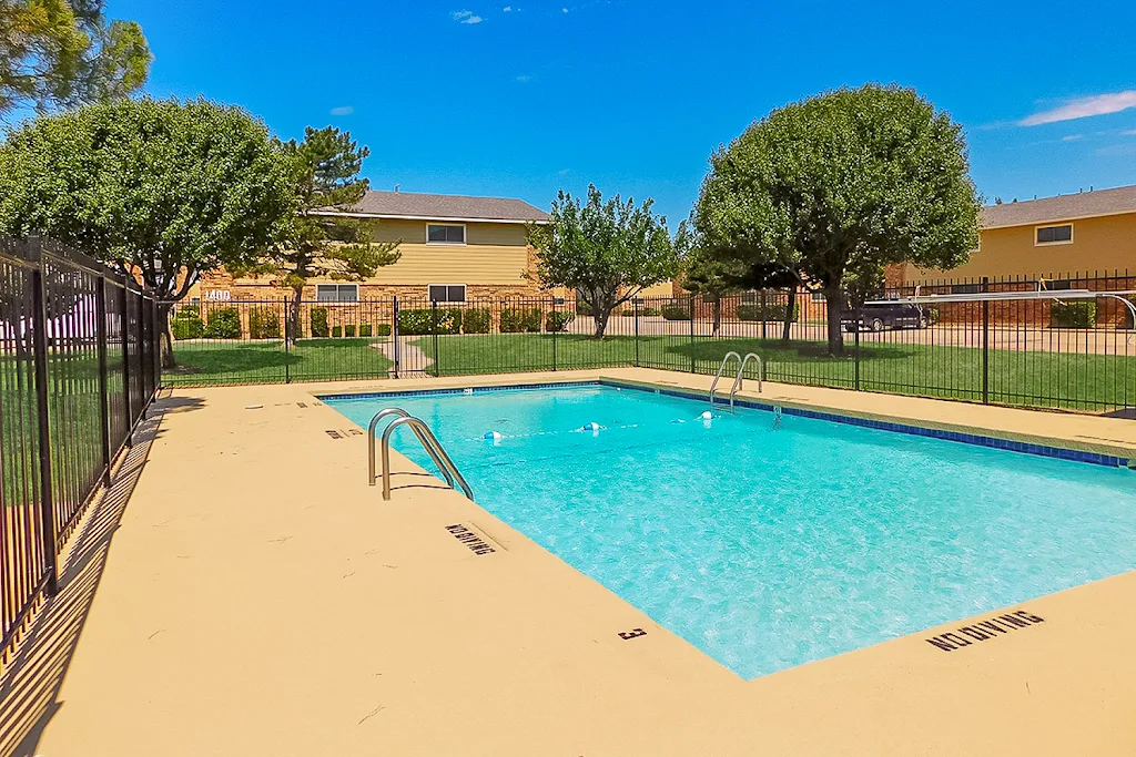 Fenced in swimming pool next to apartment buildings with trees and landscaping