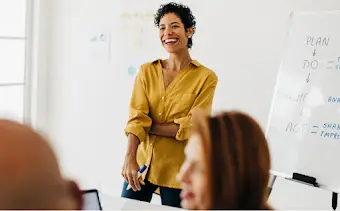 A woman at the front of a room running a whiteboard work session with her team.