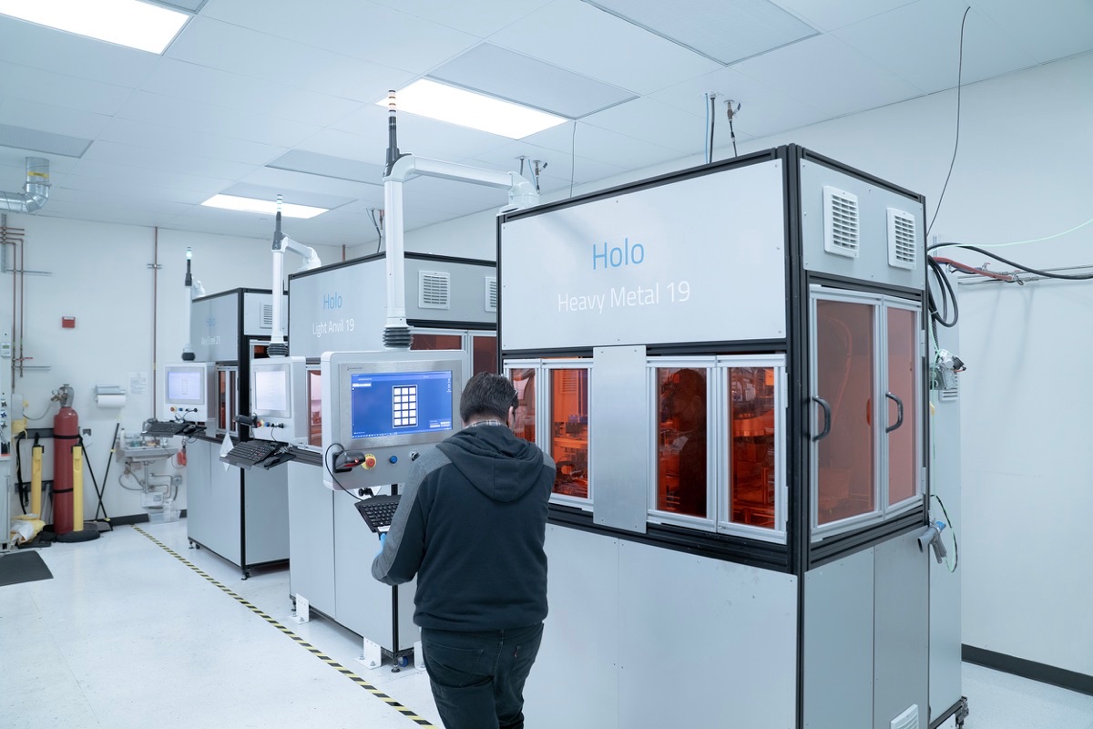 An operator standing next to one of three of Holo’s PureForm metal 3D printers from our in-house digital production fleet