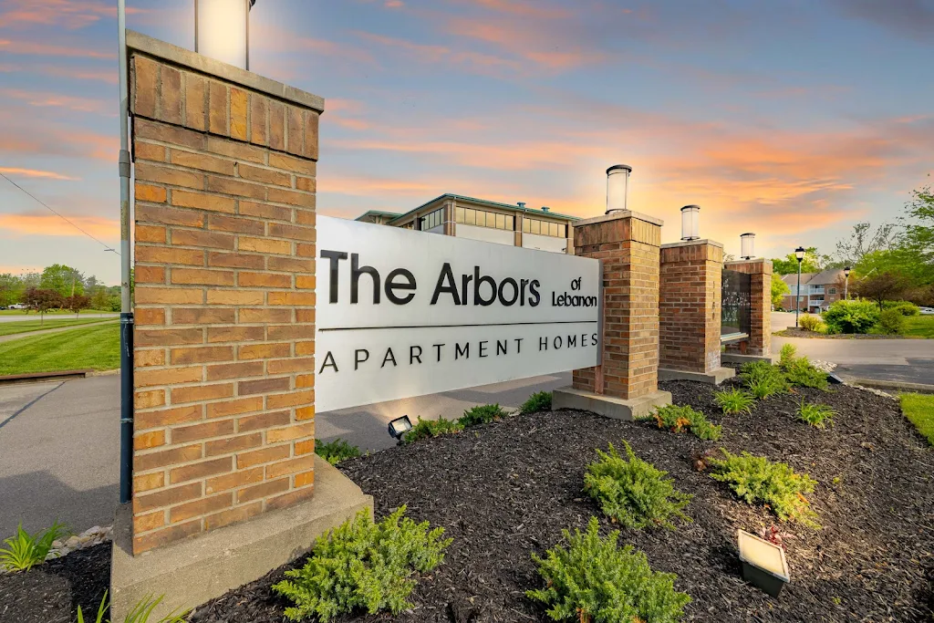 Entrance sign of "The Arbors at Lexington Apartment Homes" with landscaped garden and sunset sky.