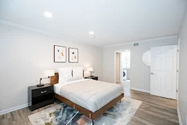 Furnished model bedroom with wood-inspired flooring, neutral walls, white trim, and modern decorative accents