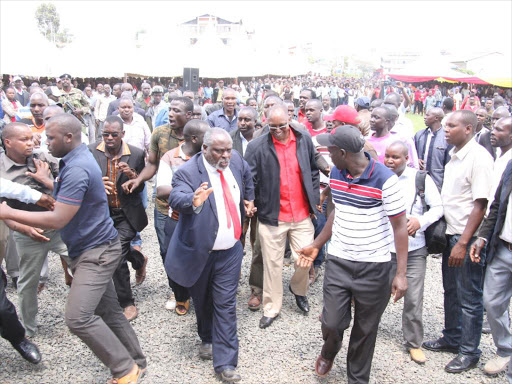 Bomet Central MP Ronald Tonui (in red shirt) is led to the dais by Jubilee county chairman Bernard Mutai at Bomet Stadium on Tuesday after youth tried to block him on claims he came to disrupt the ceremony organised by Governor Joyce Laboso /FELIX KIPKEMOI