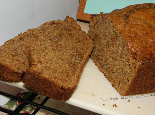 Freshly baked Oatmeal Cinnamon Banana Nut Bread loaf on cutting board being cut into serving sized slices.